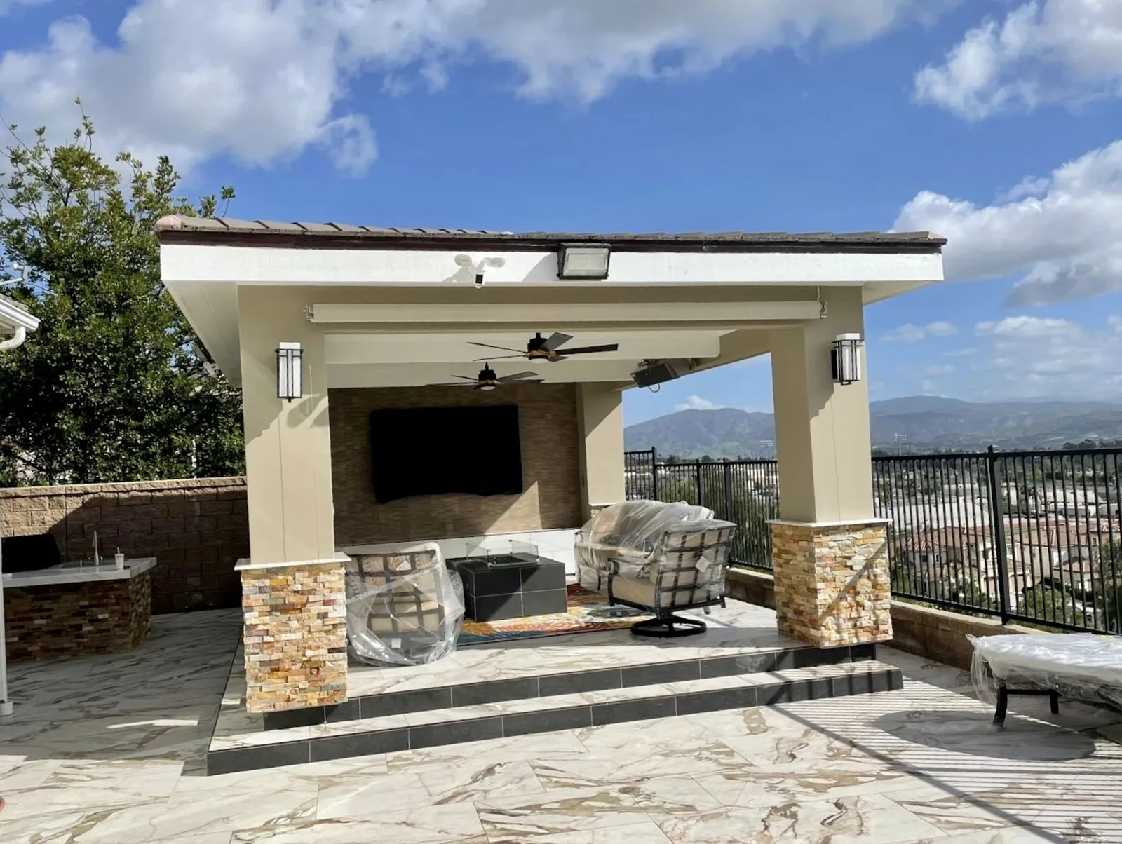 Covered patio with fireplace, TV, and lounge seating on marble tile decking in Los Angeles by Mau & Co