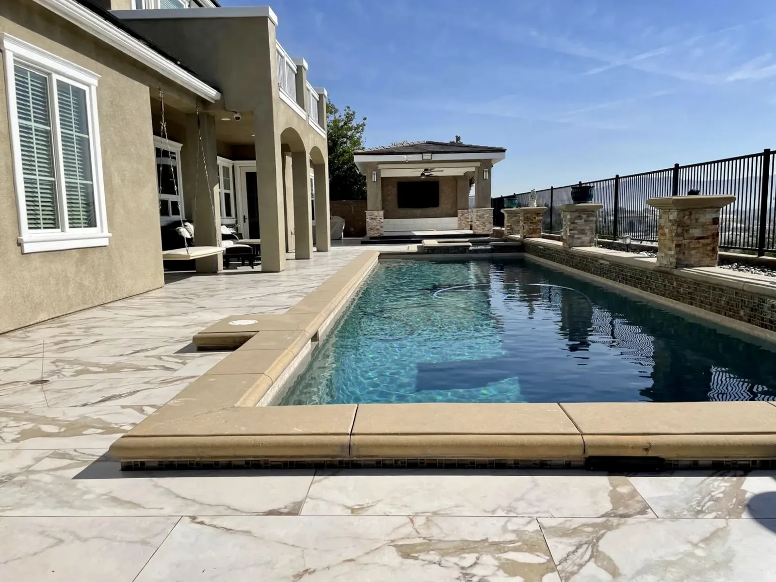 Marble tile pool deck and covered patio with outdoor kitchen at a Los Angeles home by Mau & Co