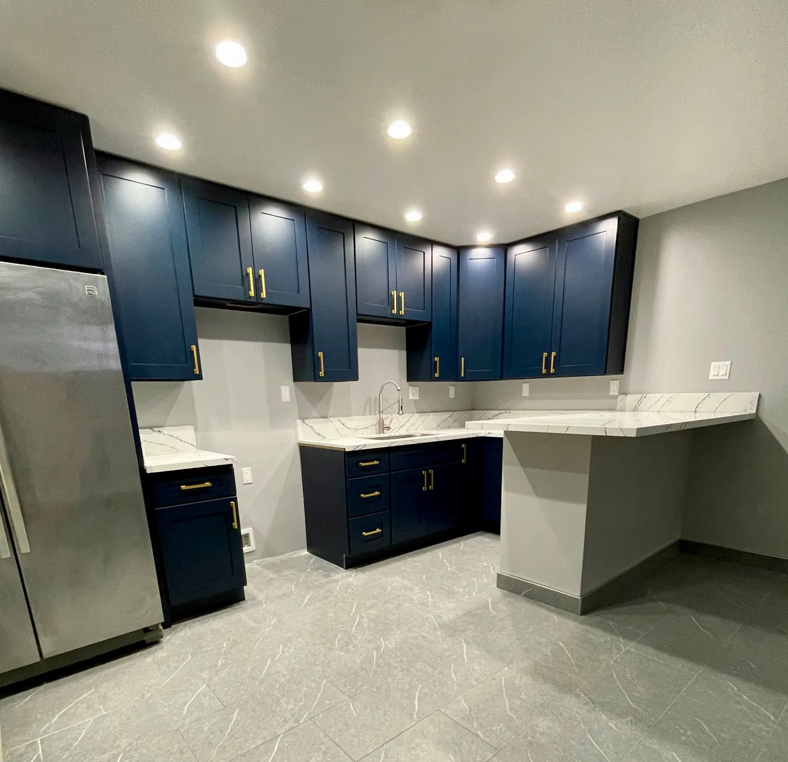 Finished kitchen remodel in a San Luis Obispo apartment complex by Mau & Co, with navy shaker cabinets, white quartz countertops, and gold hardware